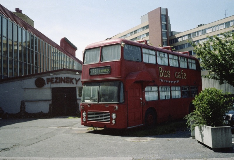 A red double-decker bus converted into a cafe, parked between buildings in daylight.