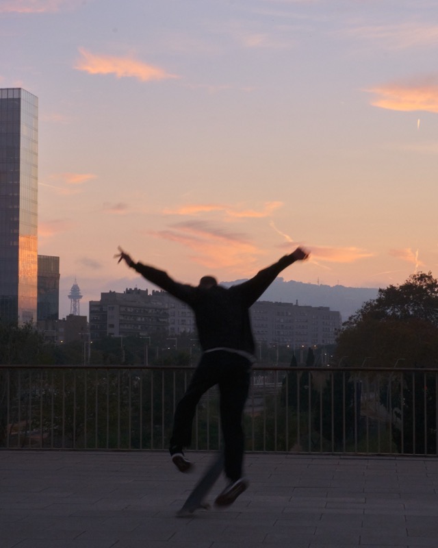 Blurred figure jumps at sunset with city skyline and clouds behind.