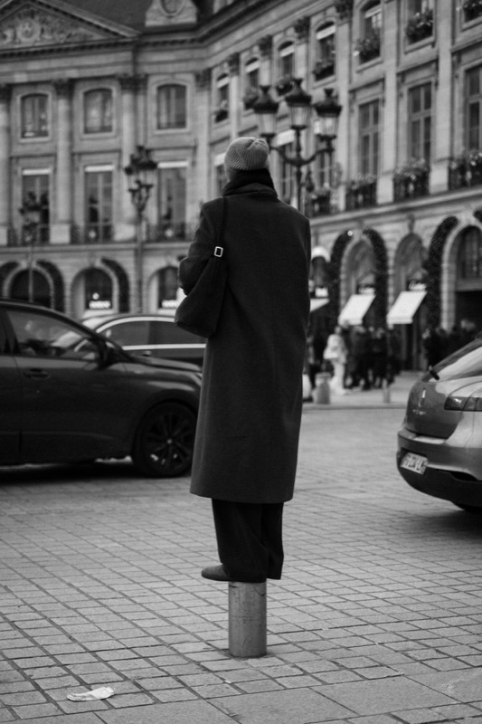 Person balances on a post in a city square, cars passing nearby.