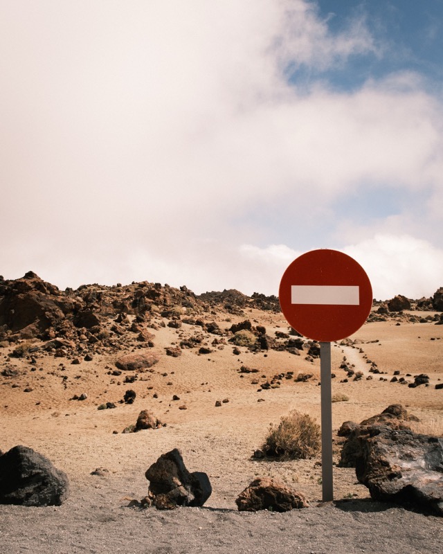 Red no-entry sign stands in a rocky desert beneath scattered clouds.