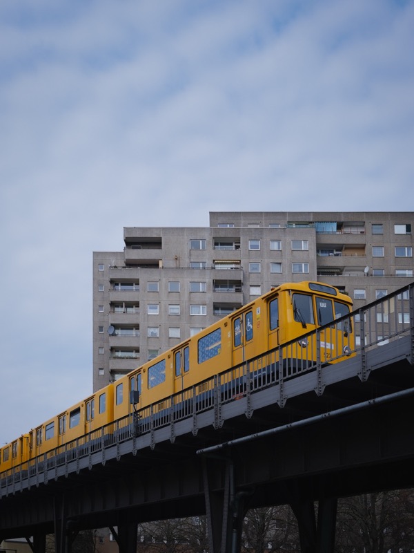 Yellow metro train passes elevated tracks in front of concrete apartment blocks.