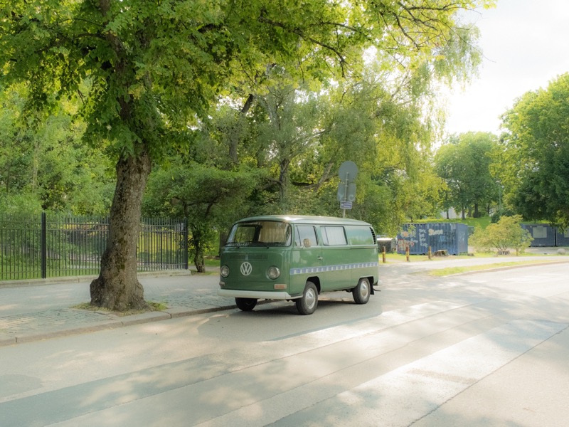 Green Volkswagen van parked under leafy trees on a quiet street.
