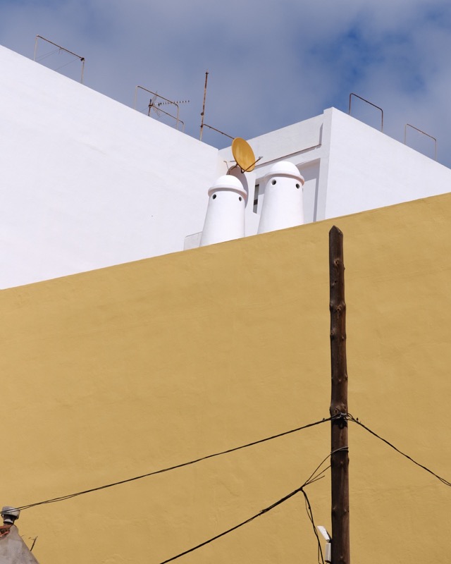 Two white chimneys peek over a yellow wall beneath a blue sky.