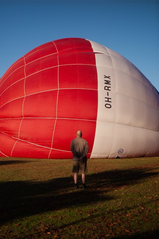 Man stands beside a giant red-and-white hot air balloon on grass.