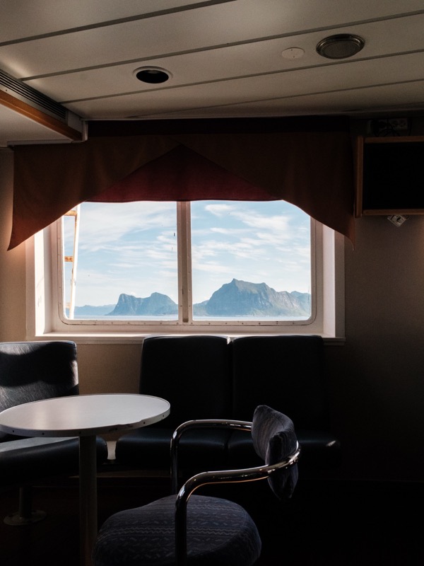 Empty ferry lounge frames distant mountains through a large window in daylight.