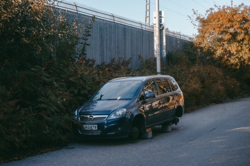 Abandoned car on blocks beside a road, surrounded by autumn bushes.