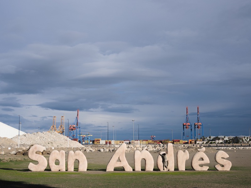 Large 'San Andres' letters sit before harbor cranes under a stormy sky.