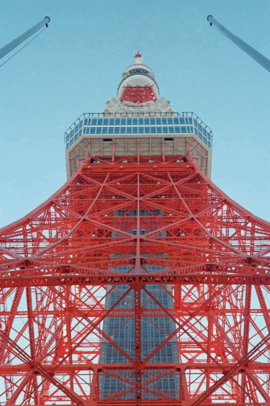 Looking up through the red steel lattice of a tall tower against blue sky.