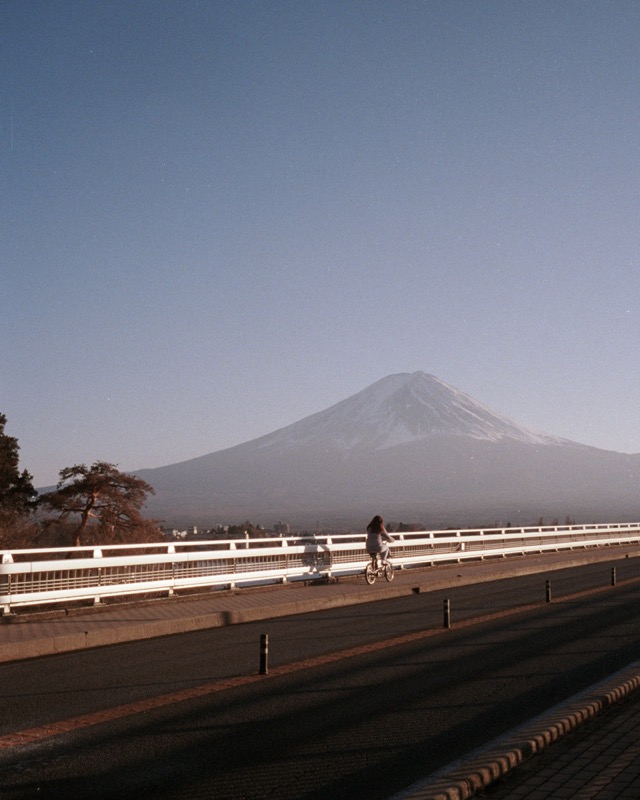 A cyclist rides along a bridge with a snow-capped mountain in the distance.