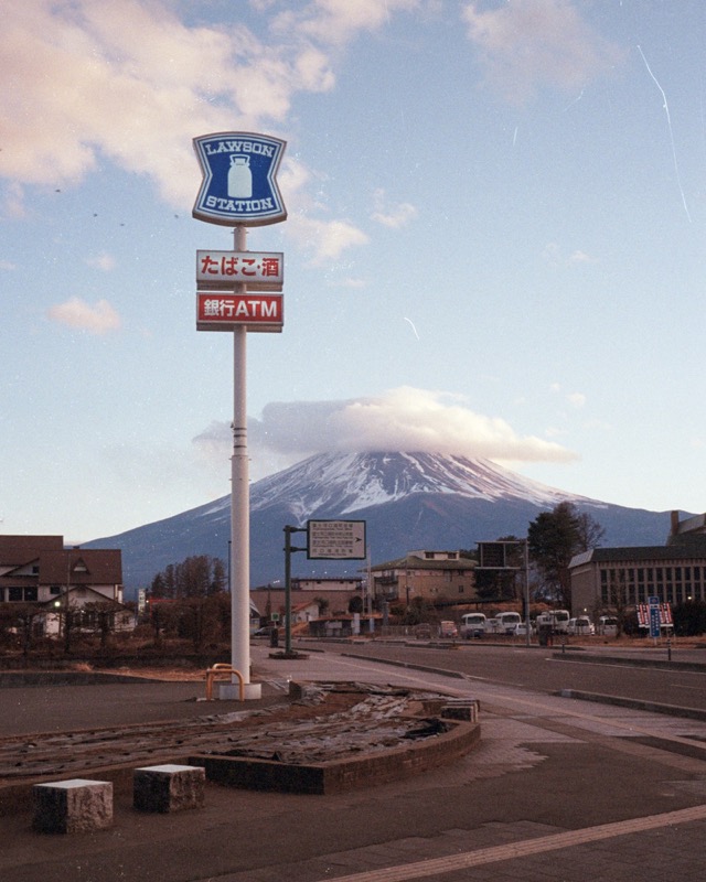 Lawson Station sign rises above a roadside town, with Mount Fuji under clouds.