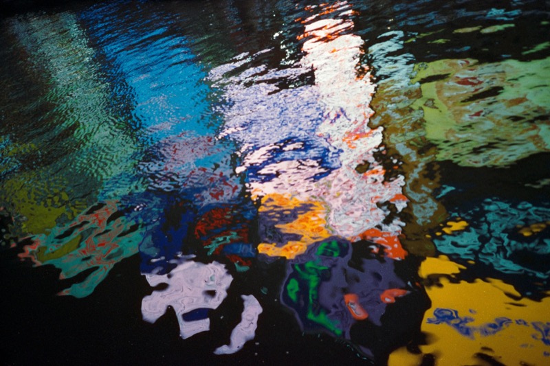 Colorful reflections ripple across dark water like abstract paint.