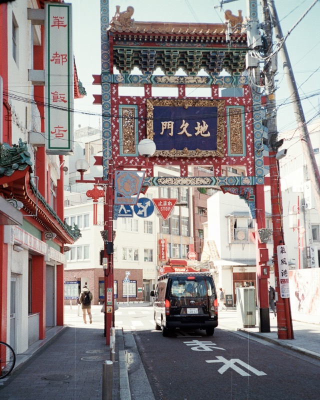 Ornate Chinatown gate spans a street, with a taxi stopped beneath it.