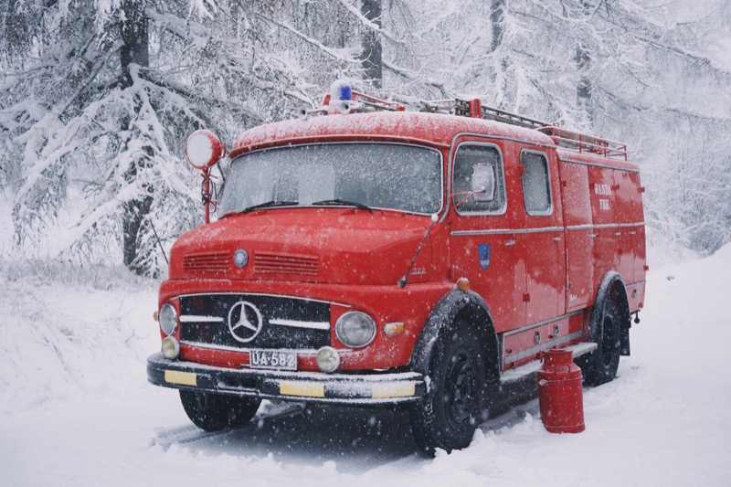 Red fire truck parked in heavy snowfall among snow-covered trees.