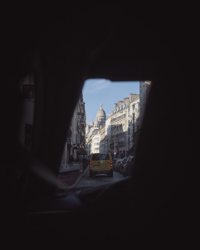 View down a city street toward Sacré-Cœur, framed by dark foreground.