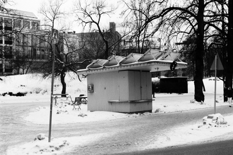 A closed kiosk with roof frames and folded awnings, set beside a snowy path.