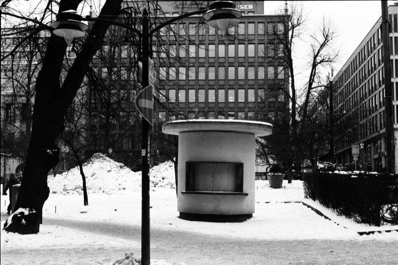 A round kiosk in a snowy plaza between office buildings, under dark street lamps.