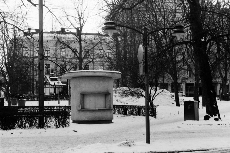 A small round kiosk in a snowy park, surrounded by street lamps and bare trees.